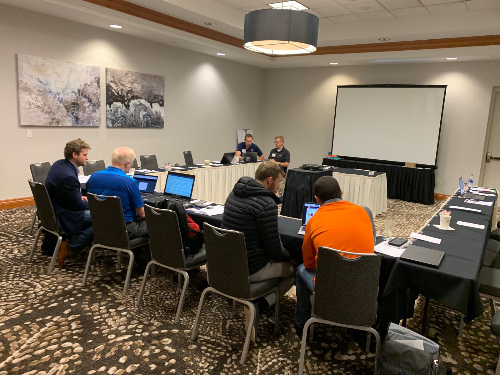 A hotel conference room with a U-shaped table; a dozen participants with laptops watch a facilitator at the front during a usability testing session.