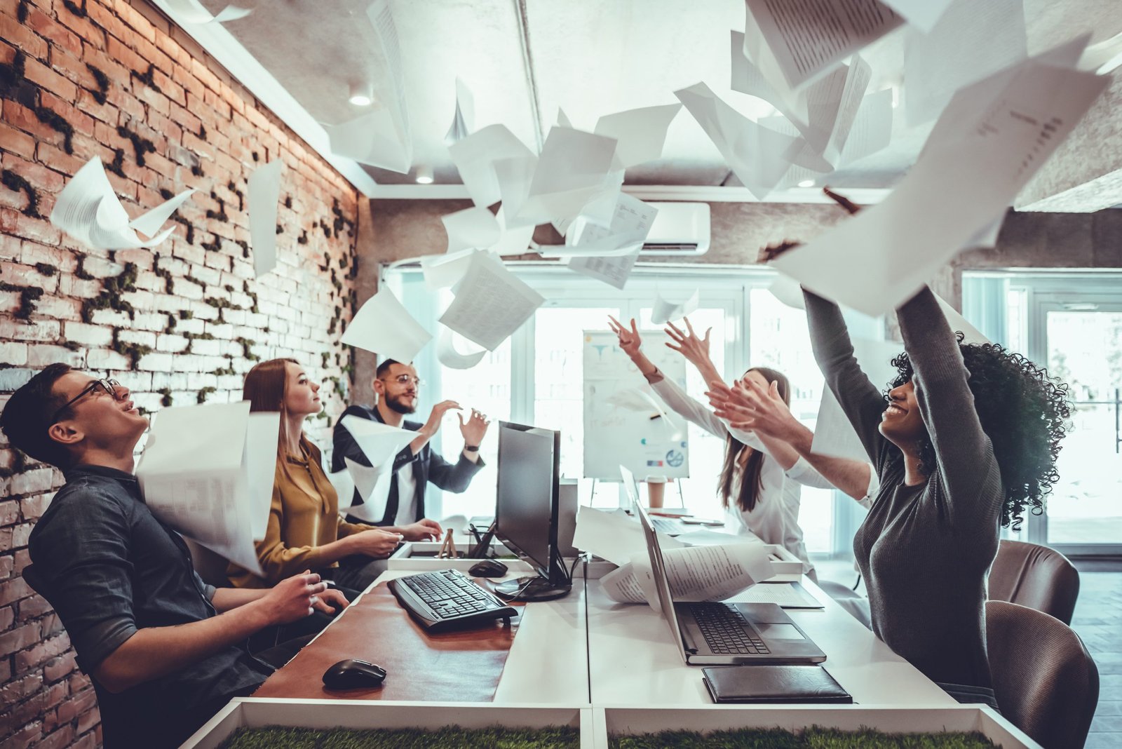 Smiling business people having fun by throwing papers in the air celebrating business success in the modern office.